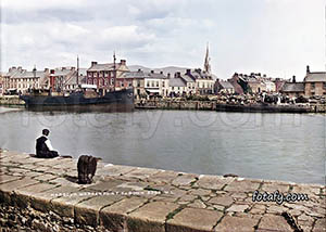 An old image that has been restored, HD enhanced and colourised of a man sitting at Warrenpoint harbour staring a the docked ships.